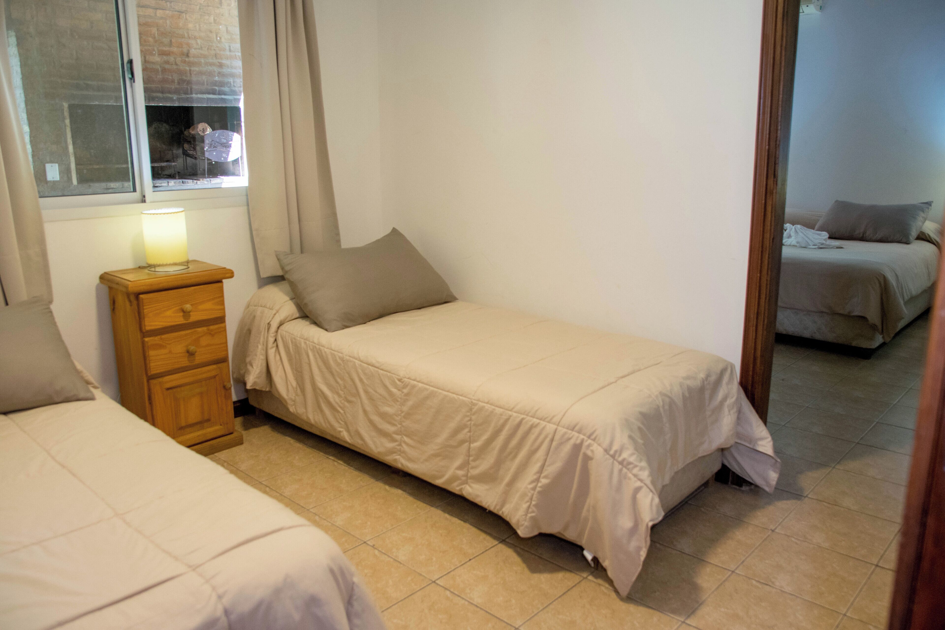 Une chambre avec deux lits simples, une table de chevet en bois avec une lampe et une fenêtre avec des rideaux.