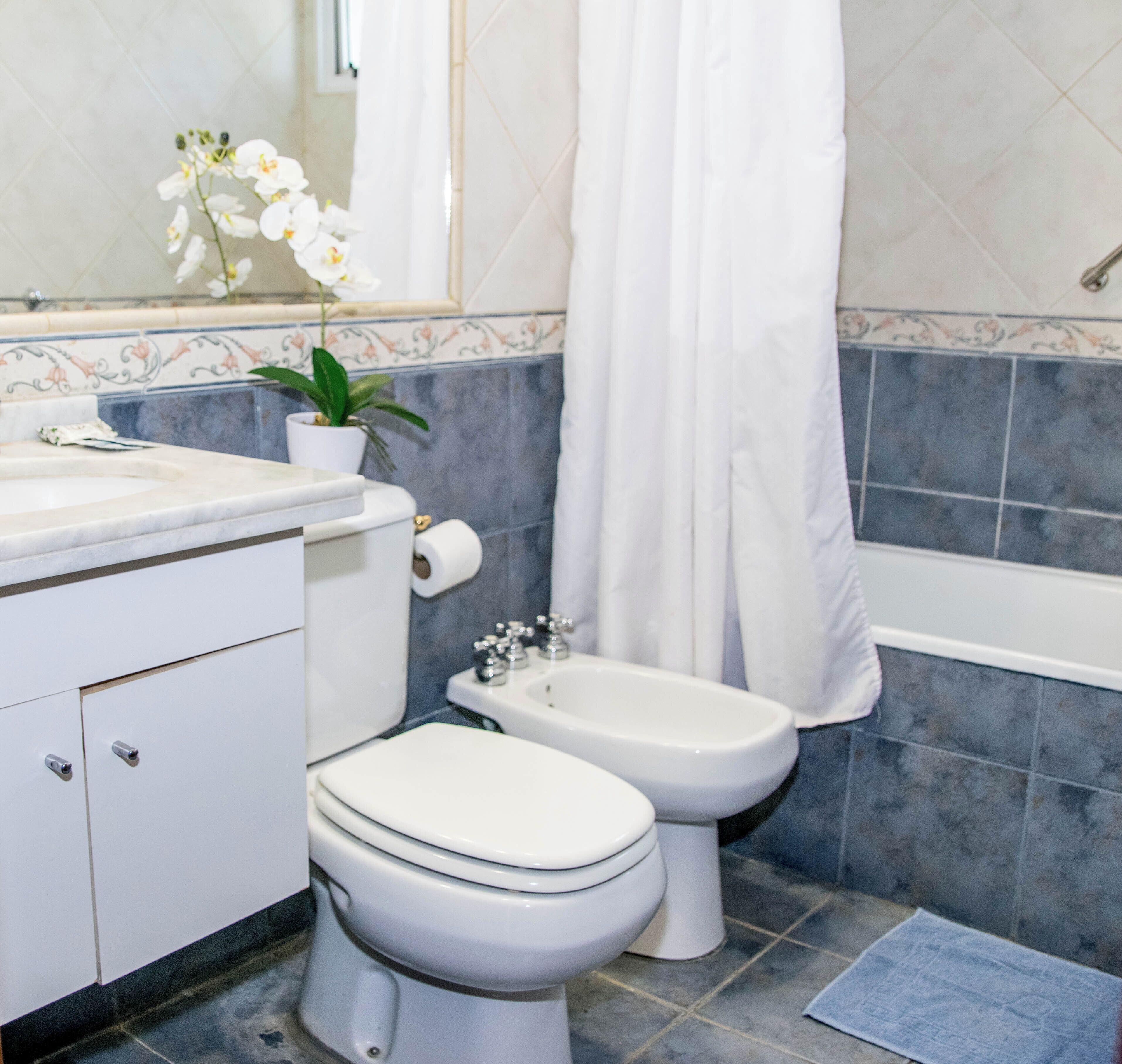 Un baño con inodoro, bidé, lavamanos y espejo.
