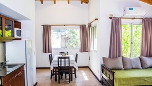 A compact room with a bed, a dining table with chairs, a small kitchen area with a sink and a microwave, and a window with curtains. - Parador 15 (Funes)