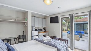 Una habitación de hotel con cama, una kitchenette pequeña, televisión y balcón con mobiliario exterior.