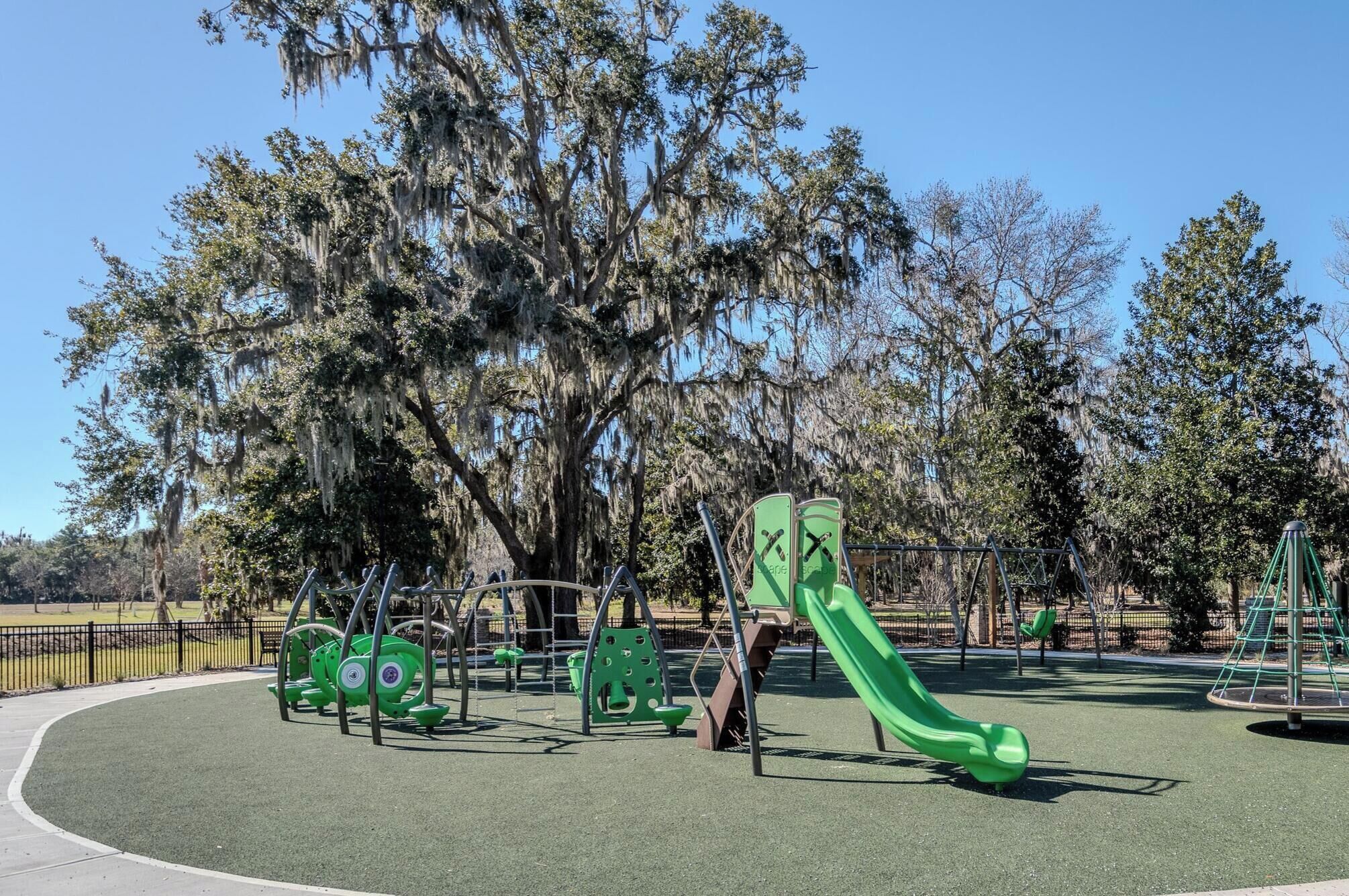 A playground with green equipment, including swings and a slide, surrounded by trees with Spanish moss.