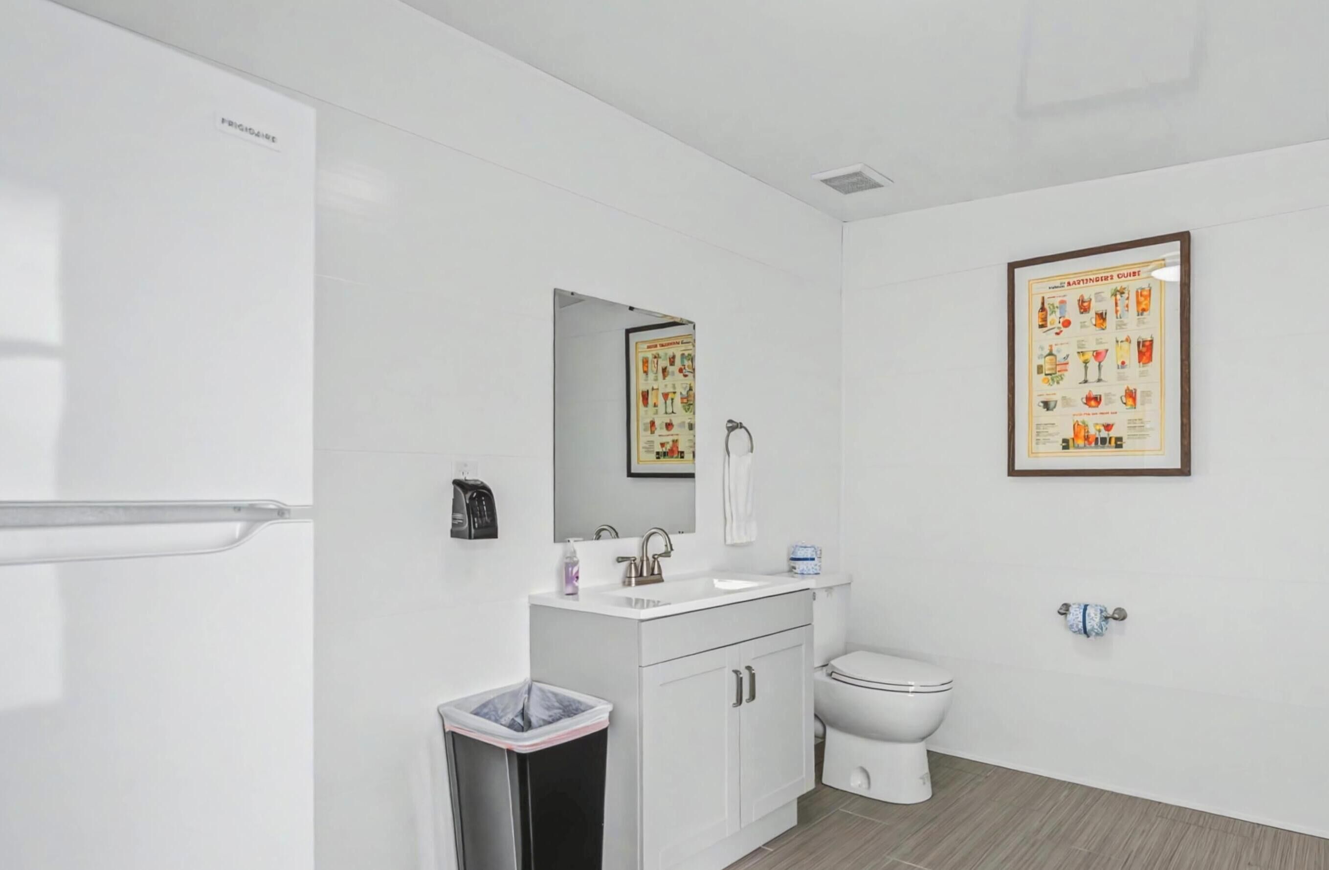 Un baño moderno con un lavabo, espejo y retrete blancos. Hay dos carteles enmarcados en la pared.