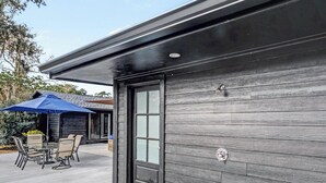 Un edificio moderno con fachada de madera oscura, puerta de vidrio y un patio amoblado al aire libre.