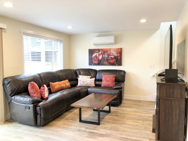 A living room with a sectional sofa, a coffee table, and a flat-screen TV on a wooden cabinet. - Entire Semi-Detached Kirkland Townhome (Kirkland)