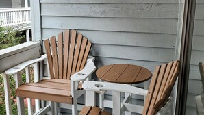 Puinen Adirondack-tyylinen tuoli ja pieni pyöreä pöytä verannalla, jossa on valkoiset kaiteet ja harmaa puuseinä.