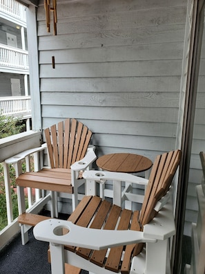 Una sedia Adirondack di legno e un tavolino rotondo su un portico con ringhiere bianche e un muro di legno grigio.