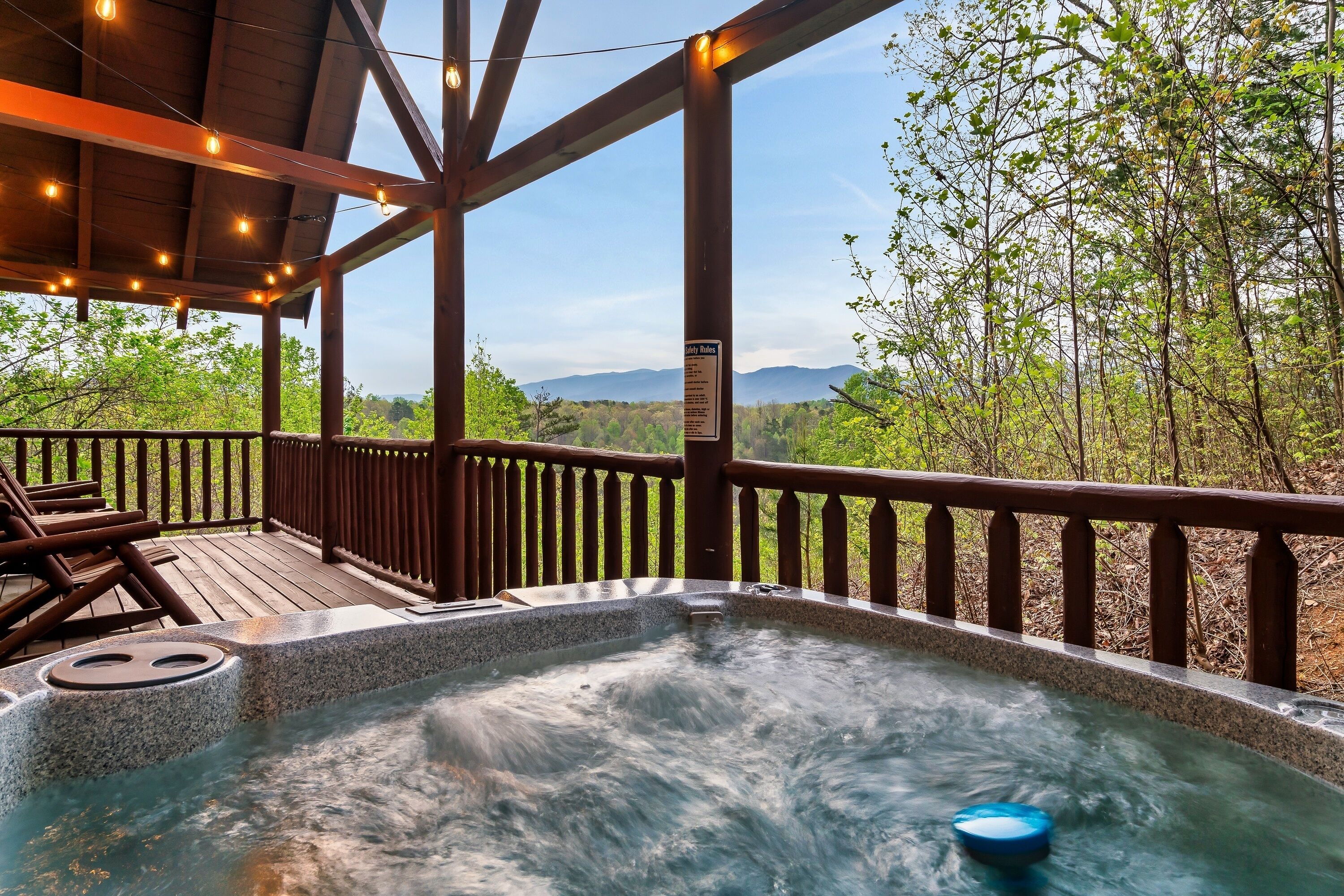 A hot tub on a wooden deck with a view of mountains and trees.