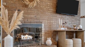 Un salon doté d’une cheminée en briques, d’un téléviseur à écran plat fixé au mur et d’une table basse en bois agrémentée d’objets décoratifs.
