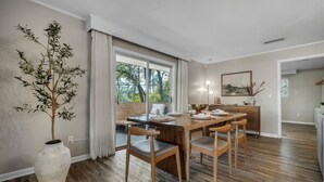Un coin repas avec une table et des chaises en bois, un vase avec une plante et une fenêtre avec des rideaux.