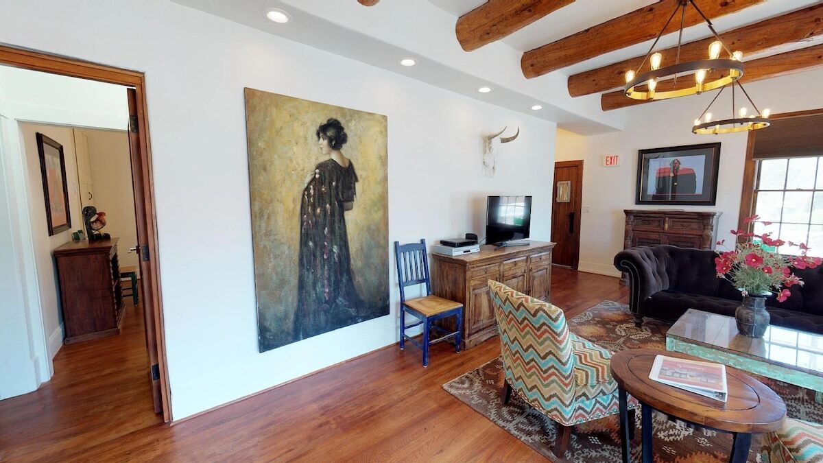 Una habitación con piso de madera, un cuadro en la pared, televisor, sofá y una silla.