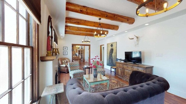A living room with a sofa, armchairs, a coffee table, a TV, wooden beams, and a large window.