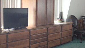 Ein Zimmer mit einem großen Holzschrank, einem Flachbildfernseher darauf und einem Sessel.