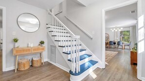 A staircase with white railings and blue steps, a console table with baskets, and a view into a dining area.