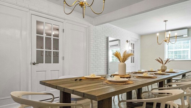 A dining area with a long wooden table set for a meal, white chairs, and a chandelier.