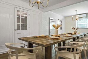 A dining area with a long wooden table set for a meal, white chairs, and a chandelier. - MAGNOLIA BARN \\ 7-8 Bedrooms \\ 8+ Parking Spots \\ 2 Miles from FSU\Capitol (Tallahassee)