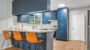 A modern kitchen with dark blue cabinets, a central island with bar stools, a window, and a white door.