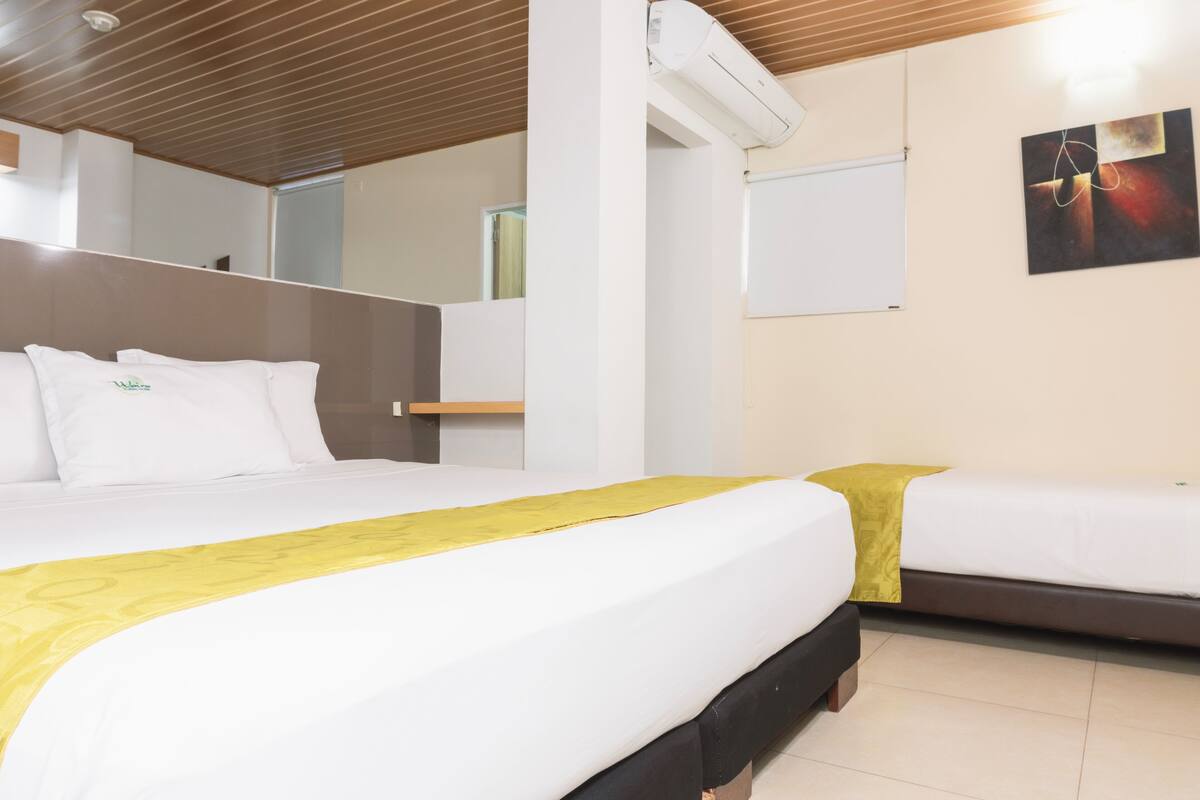 Una habitación de hotel con una cama grande, otra más pequeña, techo de madera, pared blanca y un cuadro.