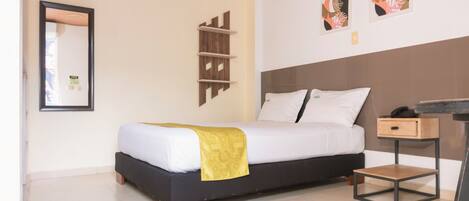Een moderne hotelkamer met een bed, nachtkastje en een klein houten krukje. Er is een wandplank en een lijst met een afbeelding boven het bed.