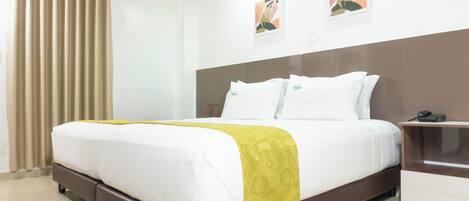 A neatly made bed with a white and yellow bedspread, a wooden headboard, and a bedside table with a phone.
