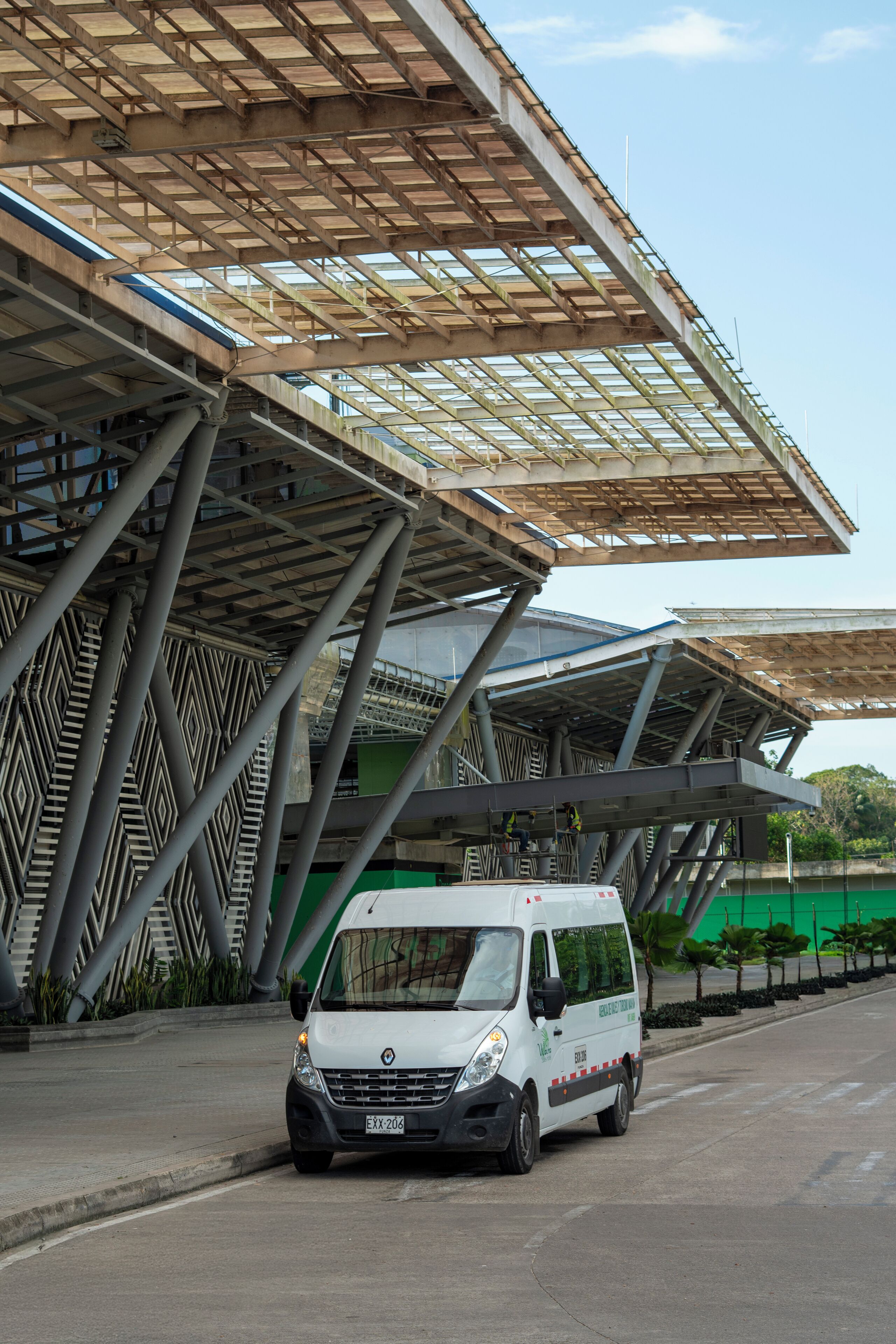 A white van parked under a modern architectural structure with a geometric design and a transparent roof.