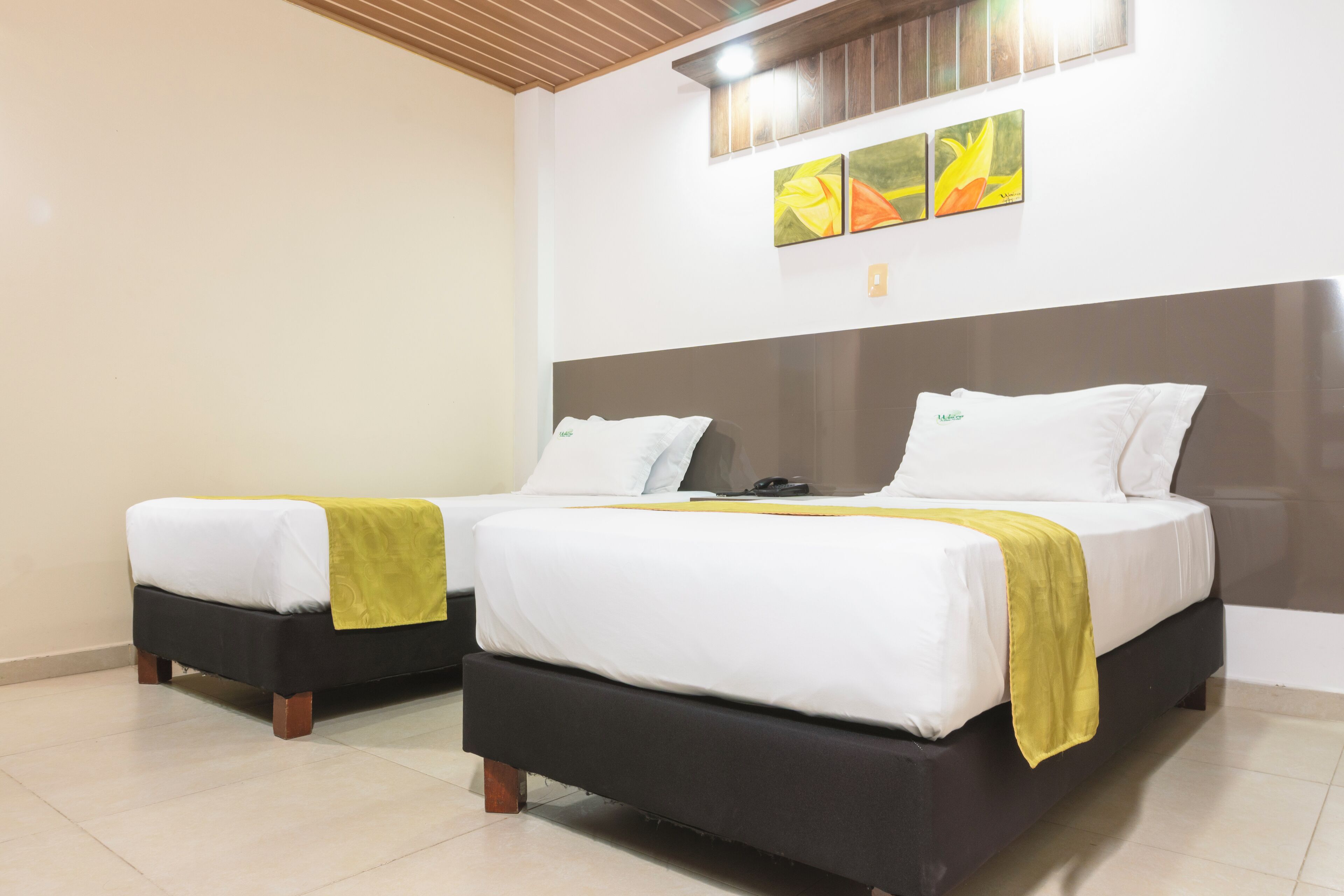 A hotel room with two beds, each with white bedding and a yellow throw. The room has a modern design with a wooden ceiling and a large window.