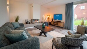 Ein modernes Wohnzimmer mit Sofa, Sessel, Couchtisch und einem flachbildfernseher an der Wand.