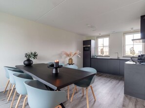 Cozinha moderna com ilha central, área de refeições com mesa escura e cadeiras azul-claras, e janela com vista para edifícios.