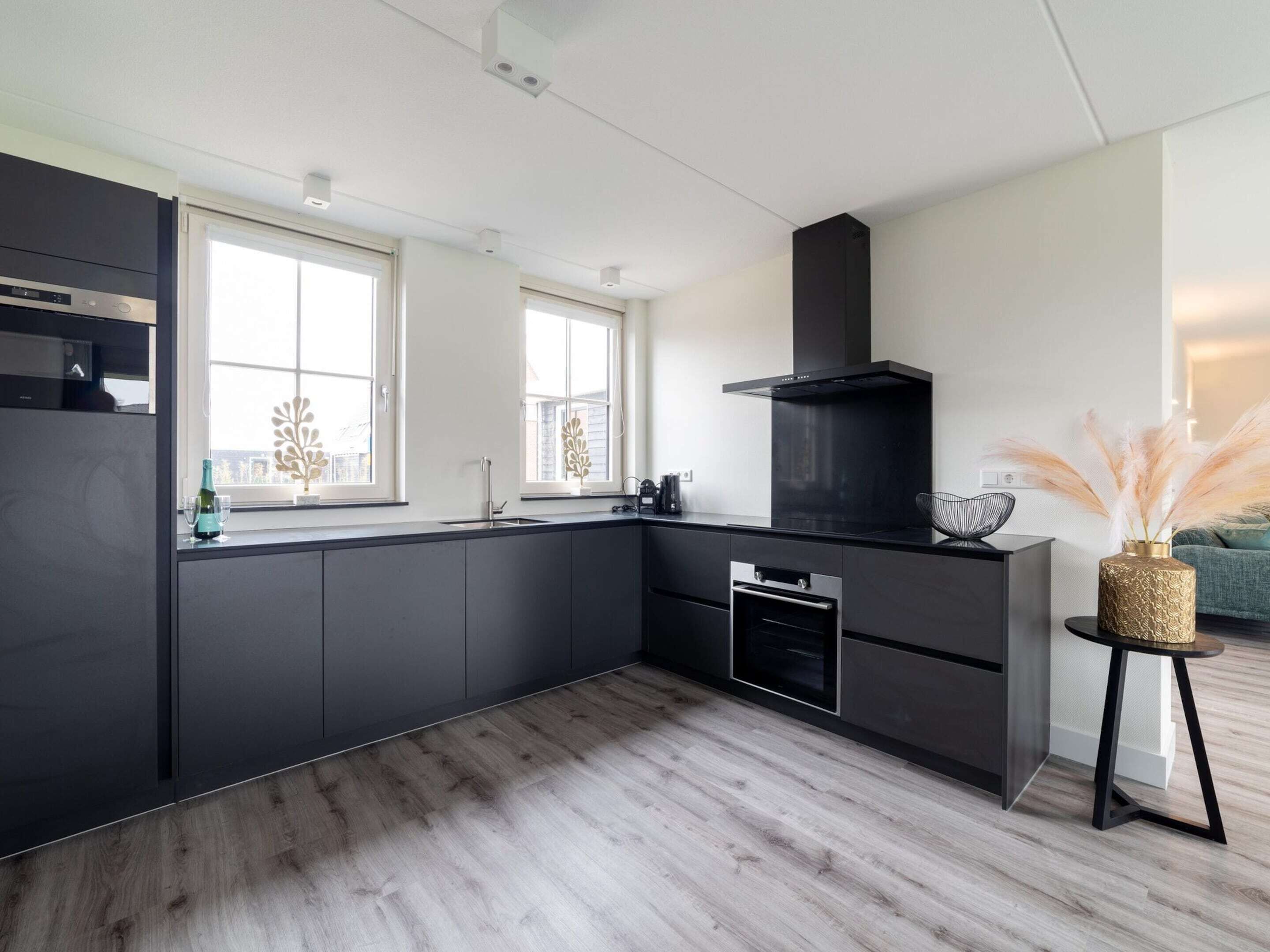 Une cuisine moderne avec des meubles de rangement aux couleurs sombres, un four encastré et une hotte noire.