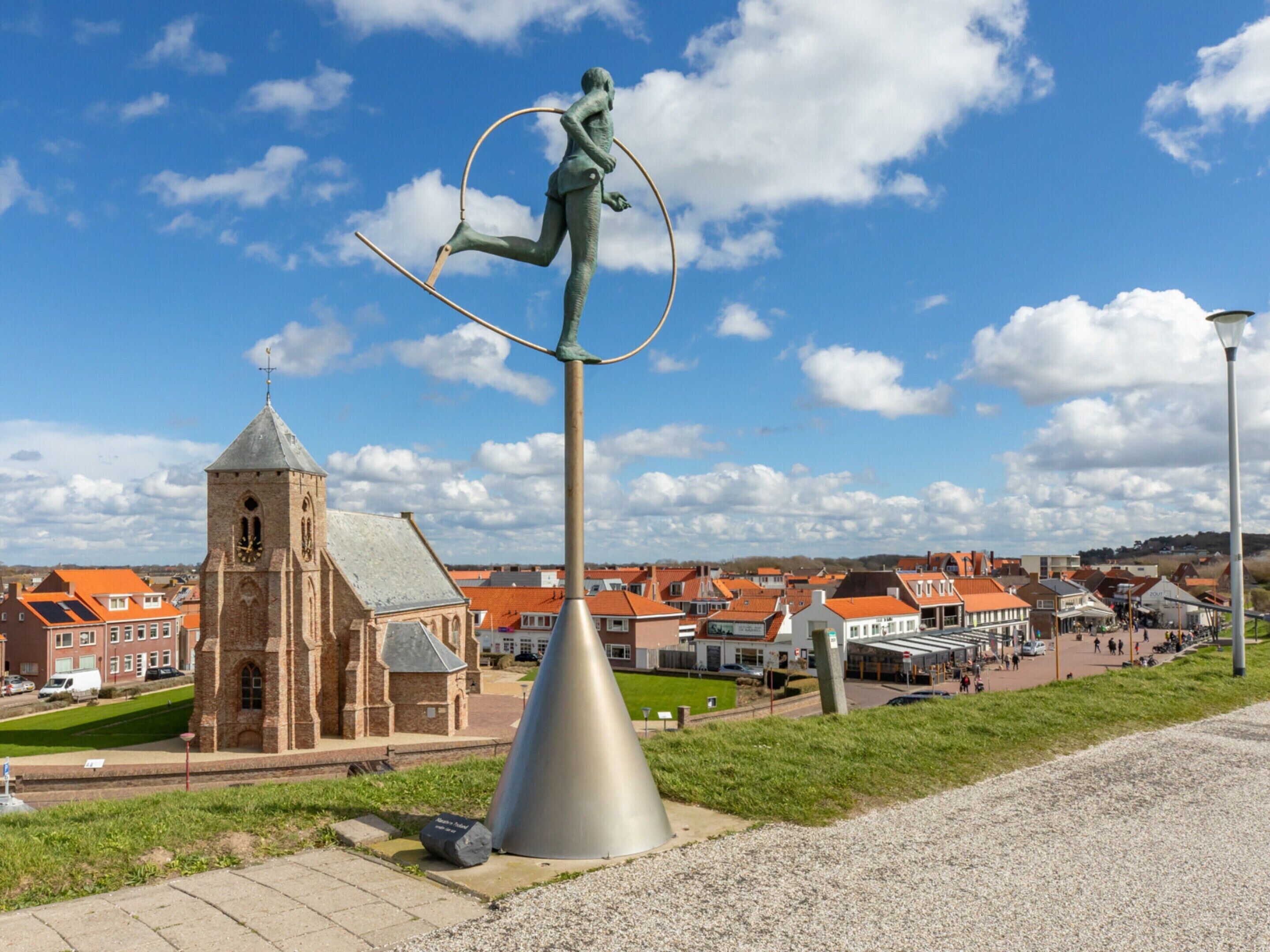 A statue of a figure balancing on a hoop, a church, and a townscape in the background.