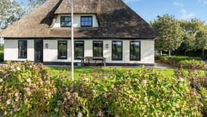 A white house with a thatched roof, a bench in front, and a well-maintained garden. - Spacious Holiday Home De Pauwenhof (Heiloo)