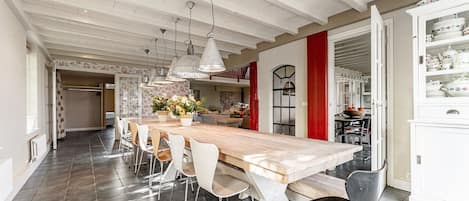 A spacious dining area with a long wooden table, white chairs, and pendant lighting.
