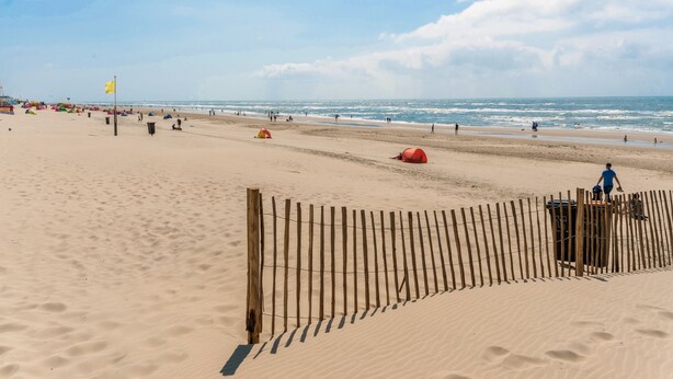 A sandy beach with a wooden fence, a yellow flag, and people in the distance. - Spacious Holiday Home De Pauwenhof (Heiloo)