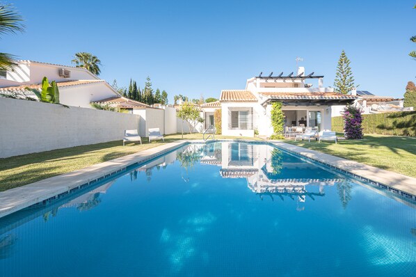 Relax by the serene pool surrounded by a well-maintained lawn and a house with a covered patio.