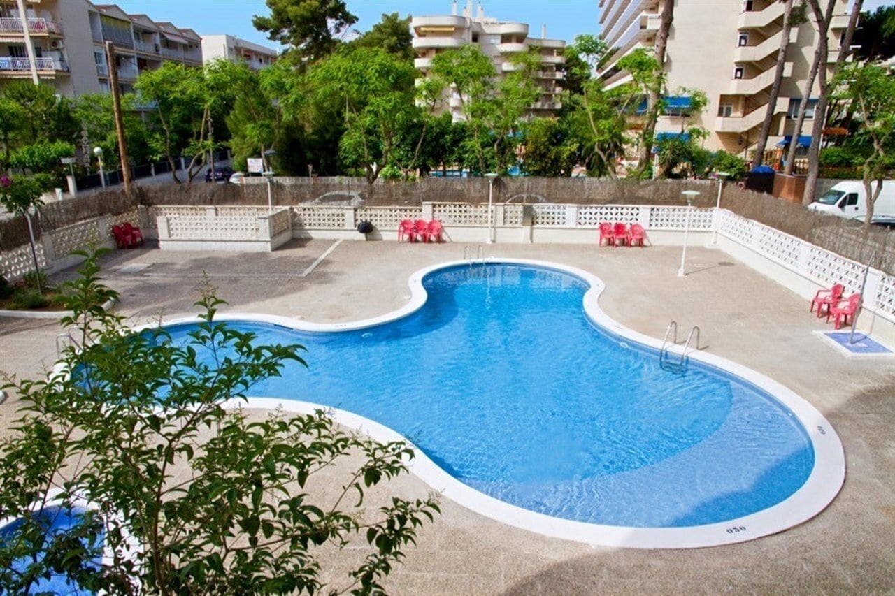 Ein Pool mit gewelltem Rand, umgeben von einem weißen Zaun und roten Stühlen.
