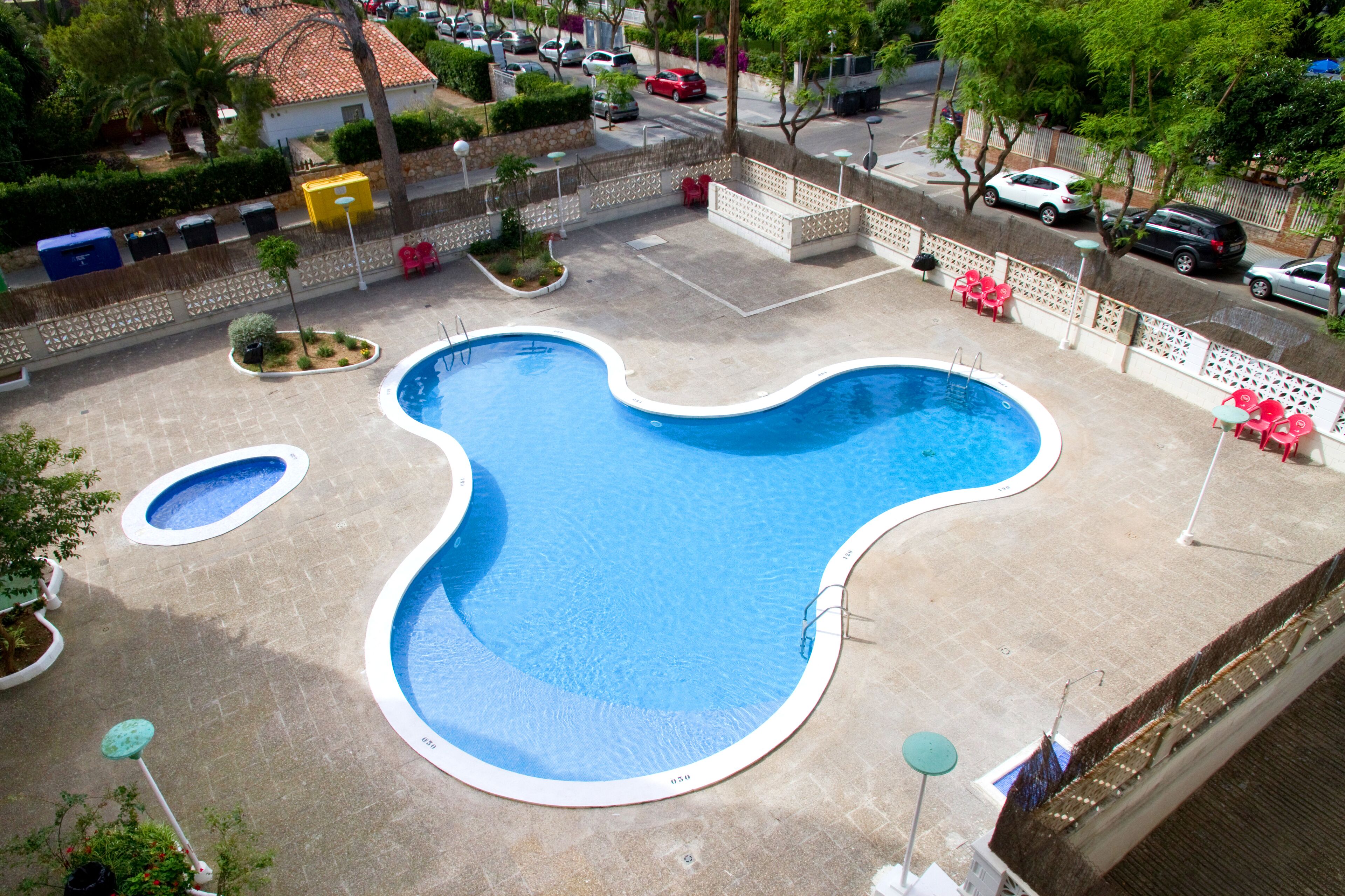 Una piscina de forma singular, rodeada por una valla y diferentes zonas de estar.