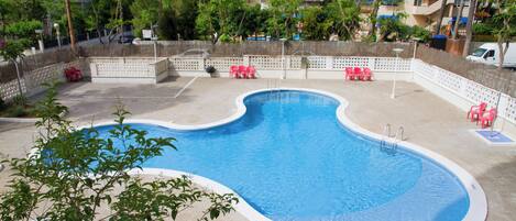 A swimming pool with a wavy edge, surrounded by a fence and trees.