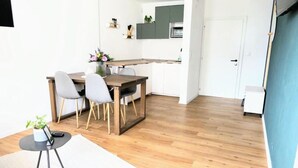 A modern kitchen with a wooden dining table, grey chairs, and a small side table with a plant. - Apartment 2- NEST'L Apartments (Mösern)