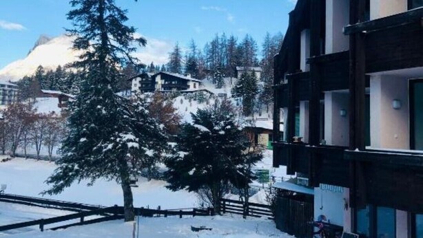 A snow-covered outdoor area with a building featuring multiple floors and balconies, surrounded by trees and a mountain in the background. - Apartment 2- NEST'L Apartments (Mösern)