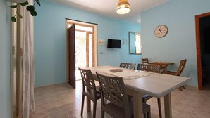 Un'area pranzo con tavolo e sedie, una lampada a sospensione, una sveglia a parete e un televisore appeso al muro.
