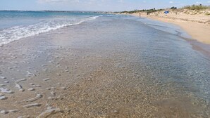 Una spiaggia con acque limpide e poco profonde, una riva sabbiosa e una costa in lontananza.