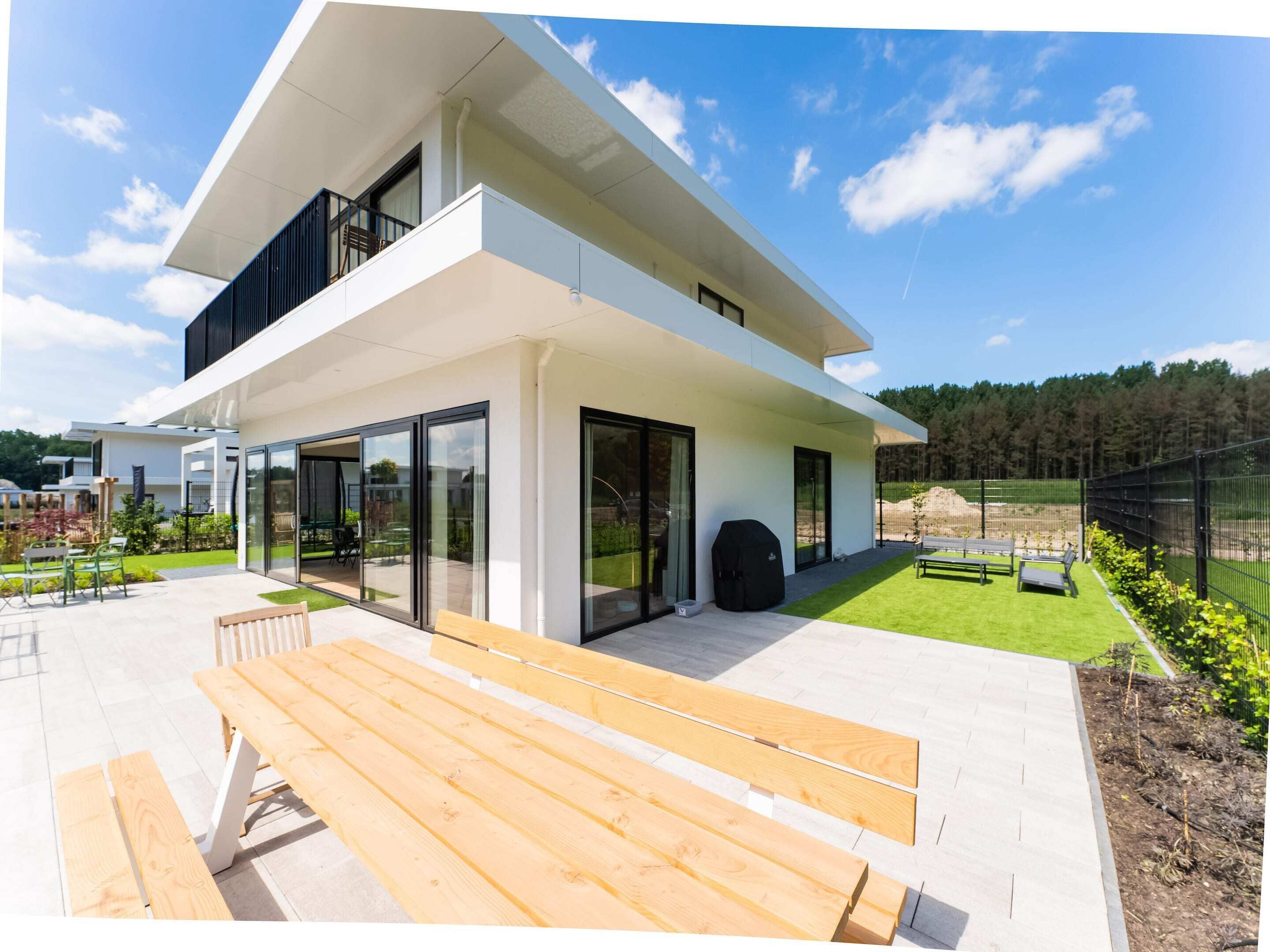 A modern two-story house with large glass doors, a wooden bench, and a well-maintained lawn.