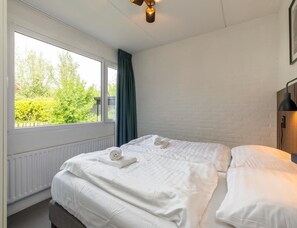 A hotel room with a large window, a bed with white linens, a brick wall, and a ceiling light fixture. - Comfort Holiday Home Near Beach (Nieuwvliet)
