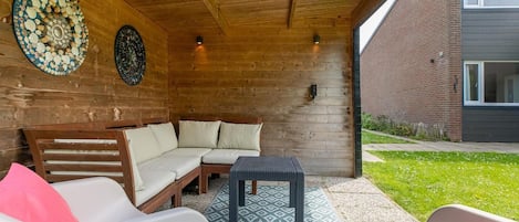 Un espace extérieur abrité avec un plafond en bois, un bâtiment en briques en arrière-plan et un tapis à motifs sur le sol.
