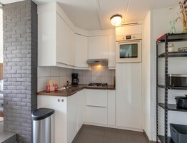 Una cocina compacta con armarios blancos, estufa a gas, cafetera y una alacena con utensilios de cocina.