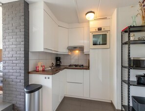 A compact kitchen with white cabinets, a gas stove, a coffee maker, and a shelf with kitchenware.