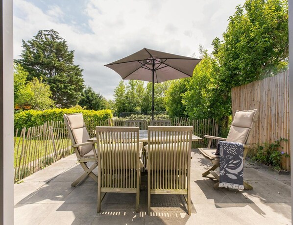 An outdoor patio with a table and chairs, a large umbrella, and a wooden fence.