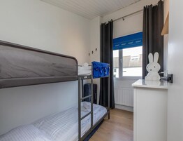 Habitación con literas, una ventana, un conejo blanco decorativo y una bolsa azul sobre el escritorio.