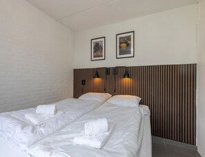 A hotel room with two beds, a brick wall, wooden panel headboard, and two framed pictures on the wall. - Comfort Holiday Home Near Beach (Nieuwvliet)