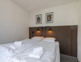 Habitación de hotel con dos camas, una pared de ladrillo, cabecero de madera y dos cuadros en la pared.