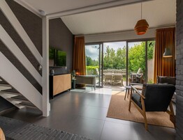Una sala de estar moderna con una escalera, un televisor de pantalla plana y vistas al exterior.